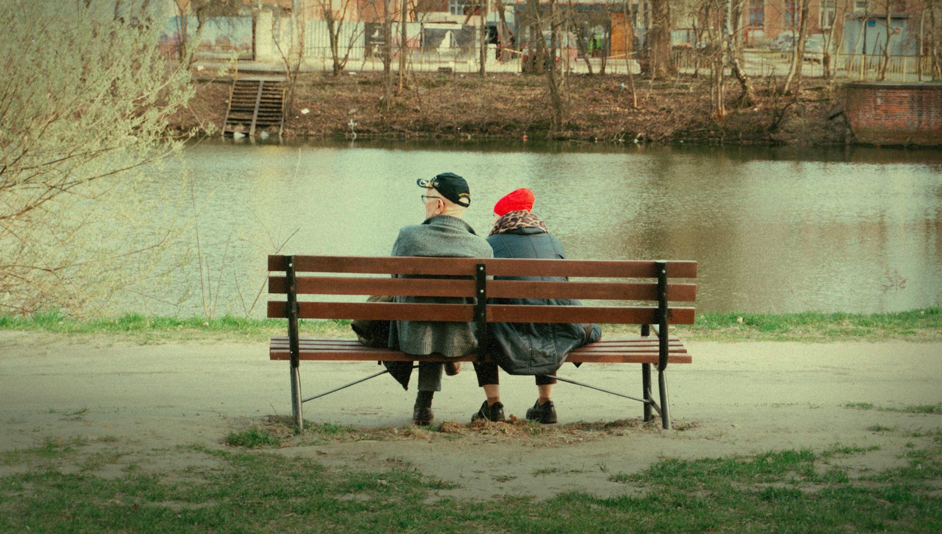 Two people sit on a park bench by the water