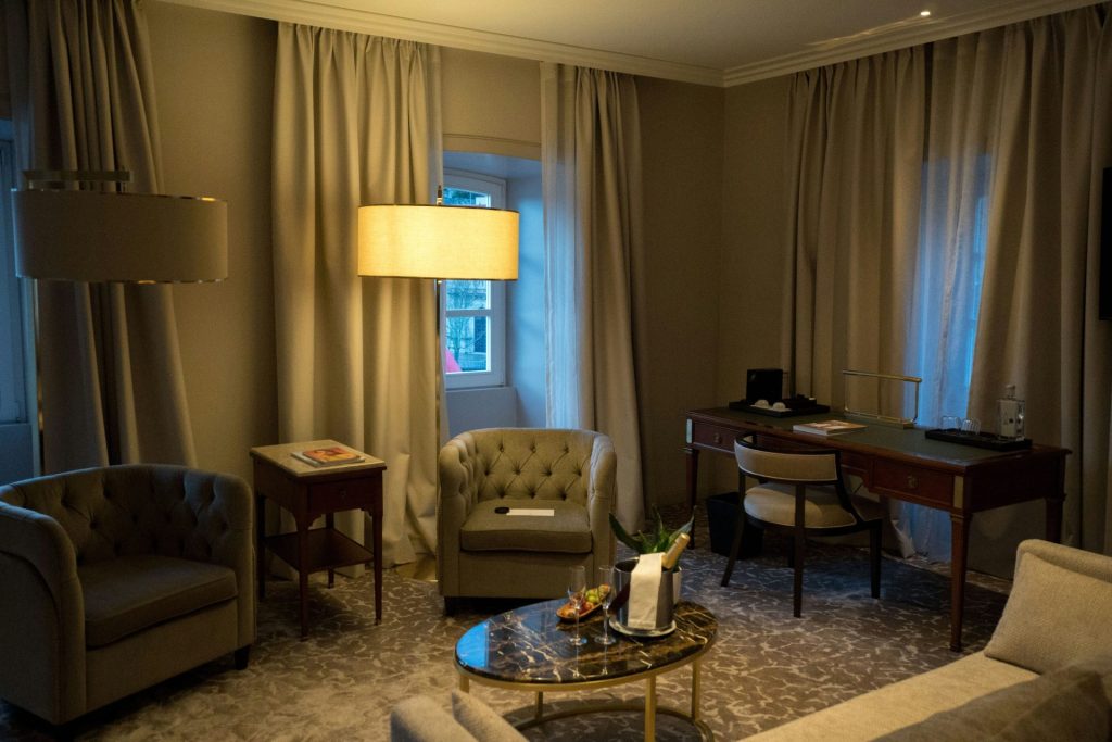 A well-lit hotel room with seating and a desk